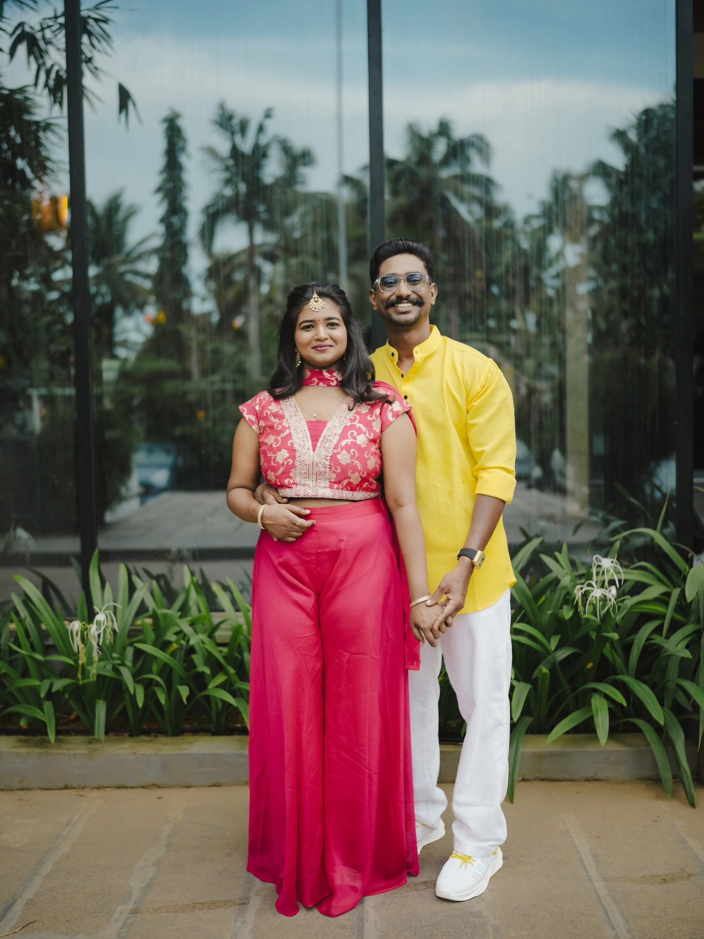 A newlywed couple standing together in front of lush greenery